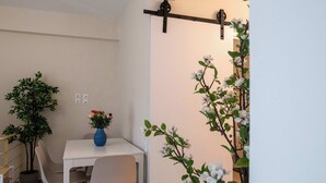 Et lille spiseområde med et hvidt bord og stole, en blå vase med blomster, samt en vægmonteret lampe.