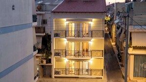 Un edificio de dos pisos con balcones, una entrada central y un pequeño jardín.
