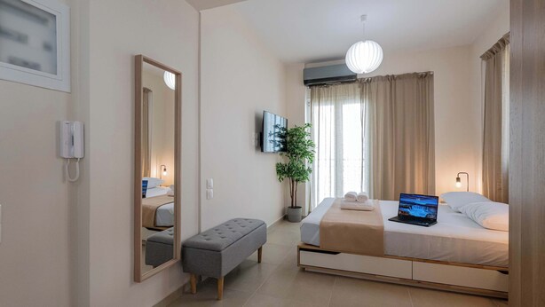 Un dormitorio moderno con una cama, un banco, una planta en maceta y un televisor.