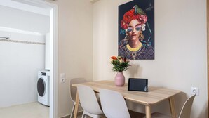Un comedor con una mesa, sillas, un jarrón con flores, una tableta y una lavadora al fondo.