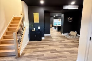 A modern interior with a wooden staircase, a black wall with a decorative piece, and a herringbone wood floor. - Moonlit Oasis (Myerstown)