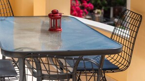 Een balkon met een tafel, stoelen, een lantaarn en potplanten.