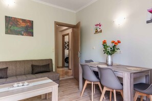 A living room with a sofa, a dining table with chairs, a vase with flowers, and a painting on the wall. - Villa Georgia 2 - A/C in All Rooms - Fast Wi-Fi - Sleeps 6 (Lefkimmi)