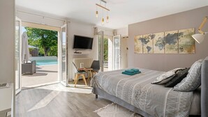 Quarto com porta aberta para área da piscina, cama com roupa de cama estampada, televisão e mapa-múndi na parede.