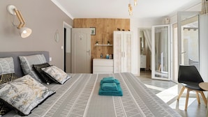 Quarto moderno com cama, mesas de cabeceira, guarda-roupa e banheiro visível por uma porta aberta.