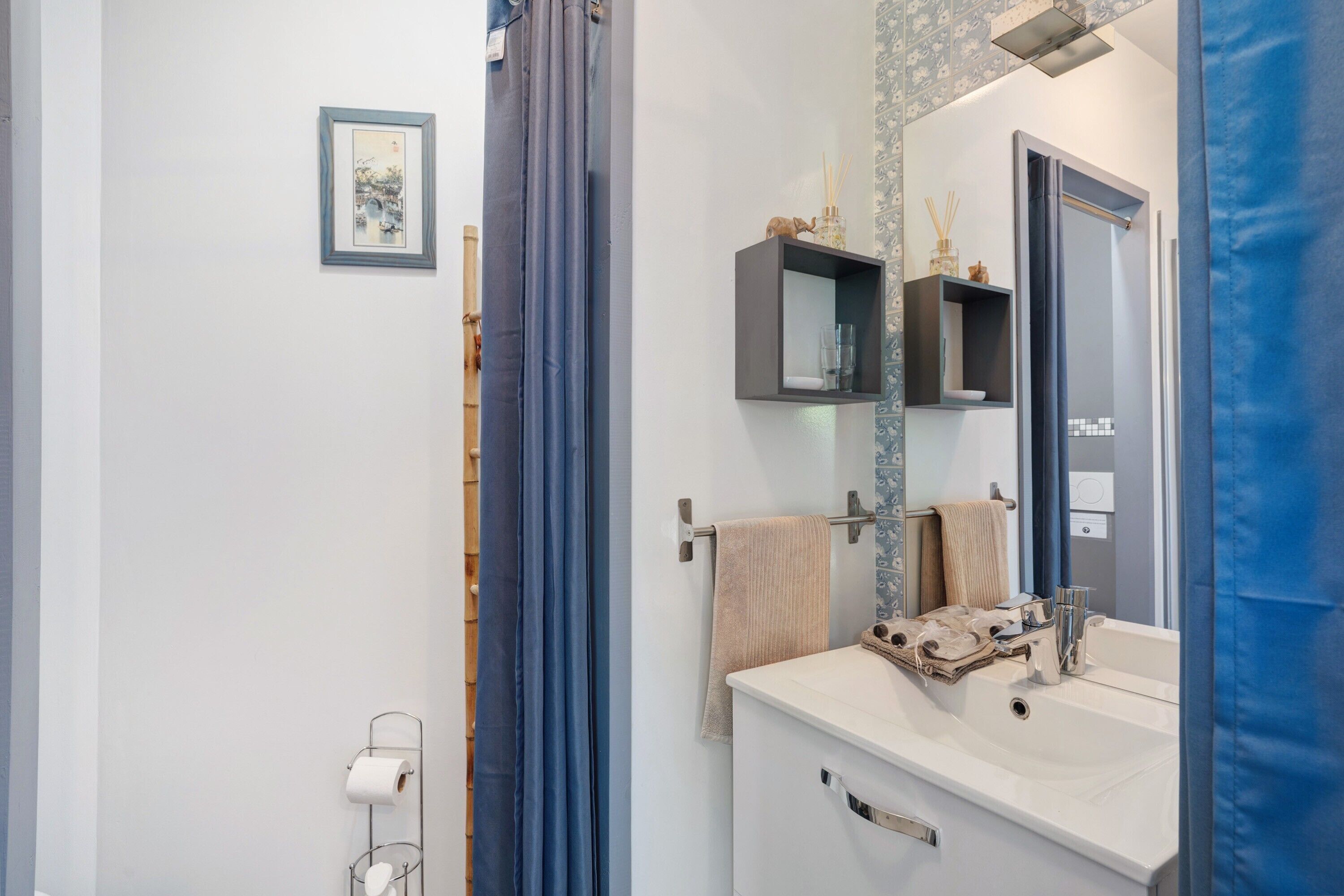 Een badkamer met een witte wasbak, een spiegel, een handdoekhouder en een wc-papierhouder.