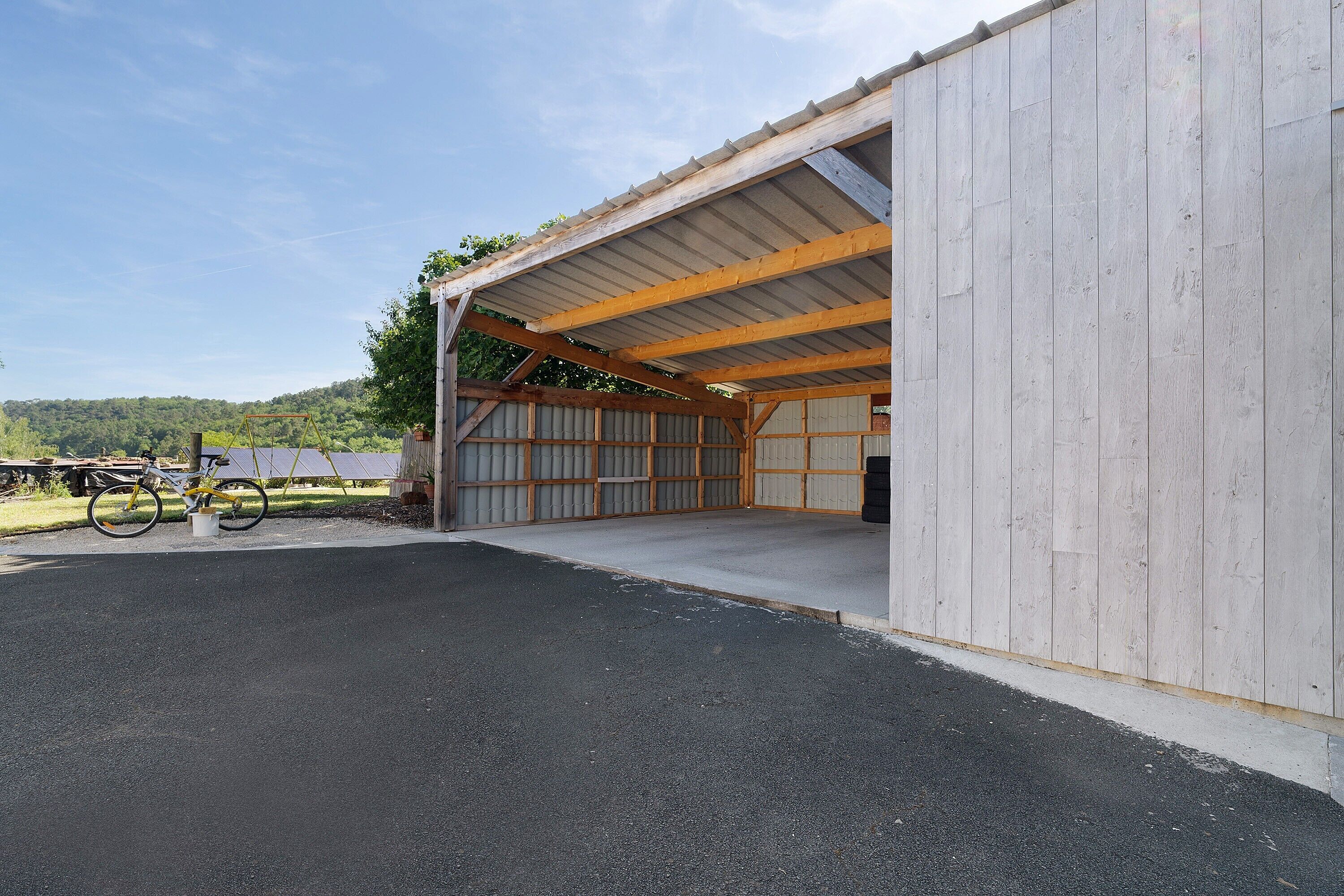 A covered outdoor area with a wooden structure, a bicycle, and a paved ground.