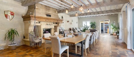 Un comedor amplio con una larga mesa de madera, múltiples sillas, una lámpara colgante y una chimenea de ladrillo.