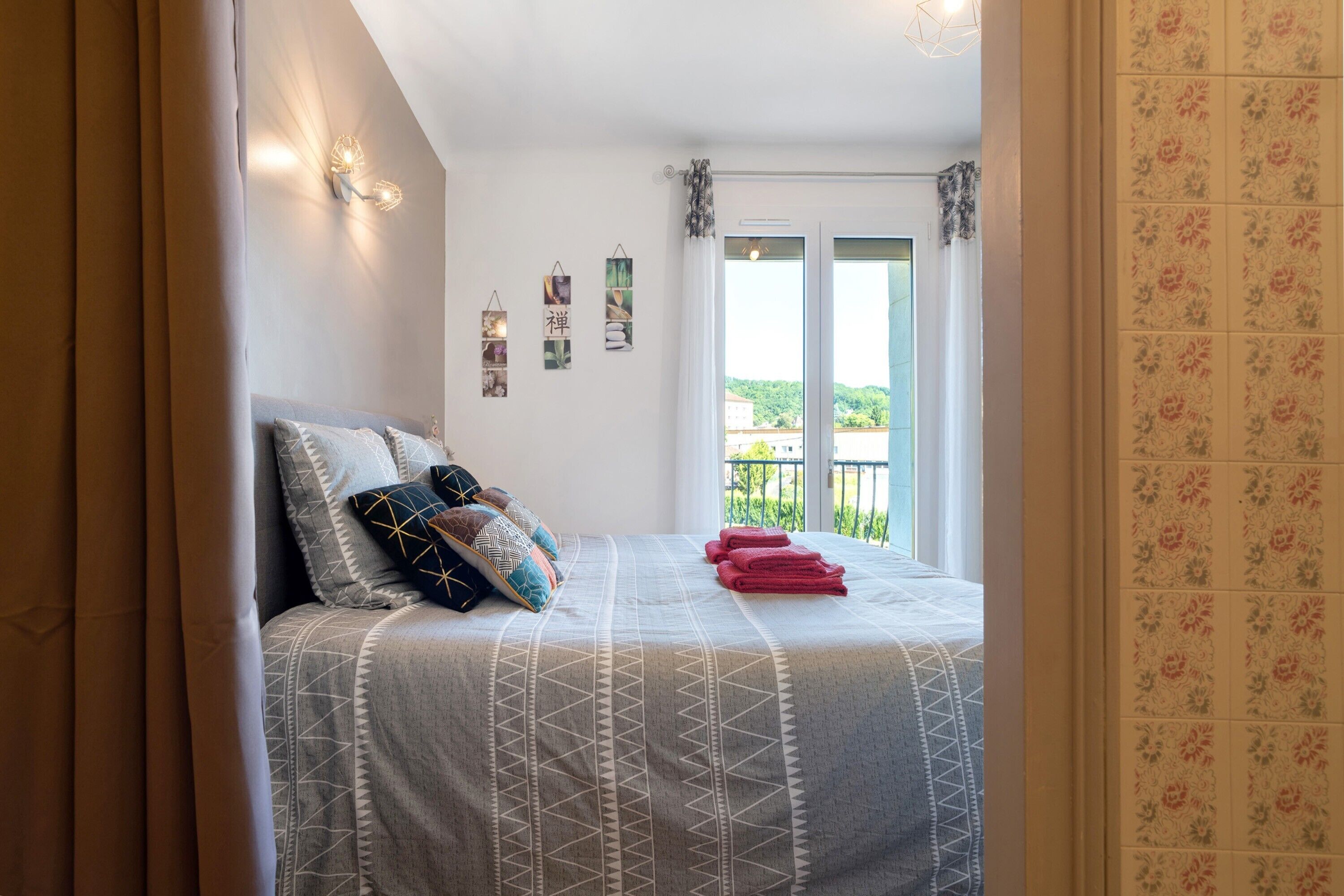A bedroom with a bed, pillows, a wall-mounted light, and a window with a view.