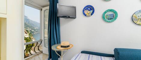 A balcony with a view of a coastal area, a TV mounted on the wall, and decorative plates on the wall.