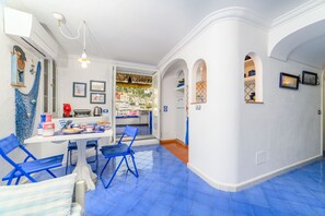 A bright room with blue chairs, a dining table, and a view of a hillside. - Esate4home - Le Vele (Positano)