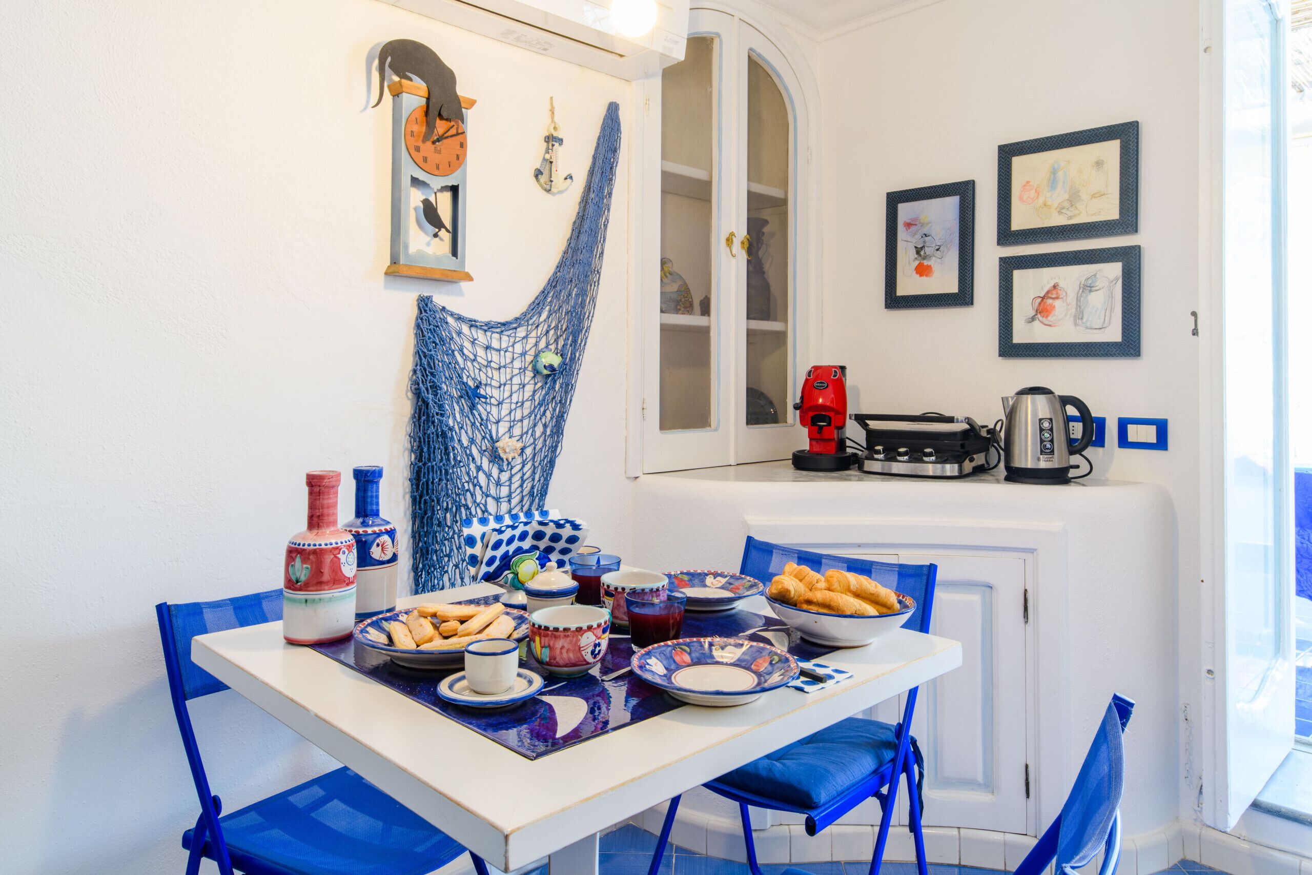 A dining area with a table set for two, featuring blue chairs and a variety of dishes and drinks.