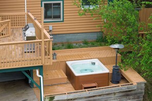 Une terrasse en bois avec un jacuzzi, un barbecue et une lanterne.