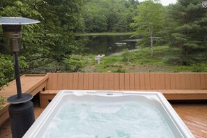 Un bain Ă remous sur une terrasse en bois, avec vue sur un lac et une forĂȘt.