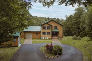 A two-story log cabin with a green roof, a front garage, and a landscaped driveway.