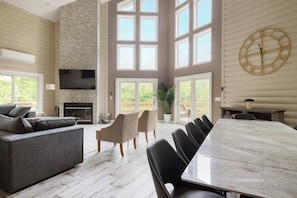 A spacious living area with a fireplace, a large dining table, and multiple windows. - Luxury Spa Lakehouse • Sauna • Steam Room • Gym (Swan Lake)