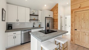 A modern kitchen with white cabinets, a stainless steel refrigerator, a built-in oven, and a grey countertop island with stools. - The Keowee Hideaway• Lakefront • 25 min to Clemson (Seneca)