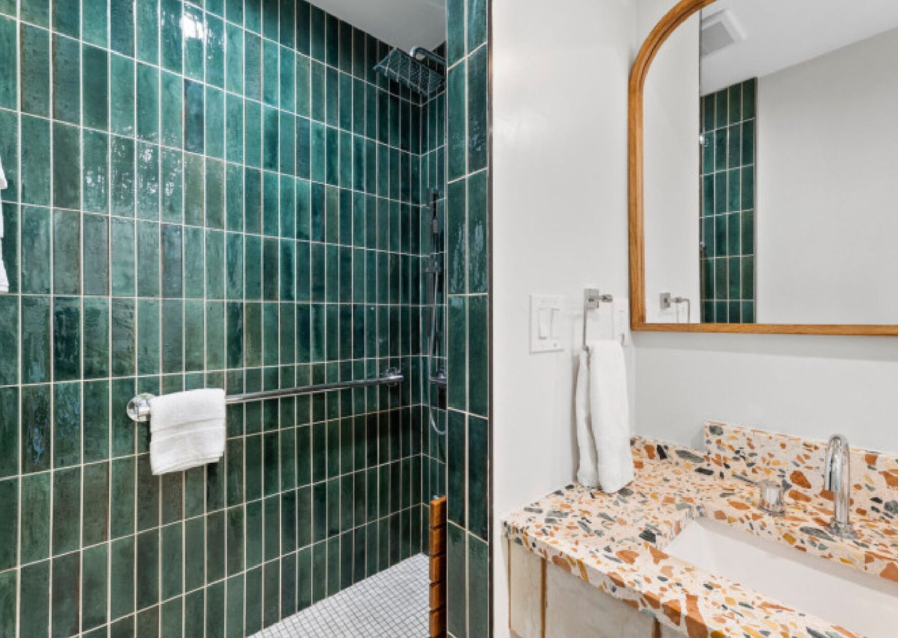 Un baño con paredes de azulejos verdes, ducha, lavamanos con encimera de mosaico y espejo.