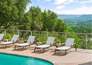 A poolside area with lounge chairs and potted plants, overlooking a forested landscape. - Amazing King Room (ADA Accessible) - Bygone Hotel (Wimberley)