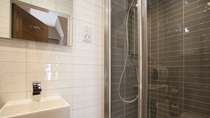 Un baño con lavamanos blanco, espejo y cabina de ducha con paredes de vidrio.