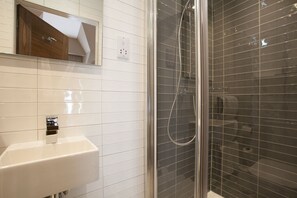 Une salle de bain avec un lavabo blanc, un miroir et une douche séparée par une paroi de verre.