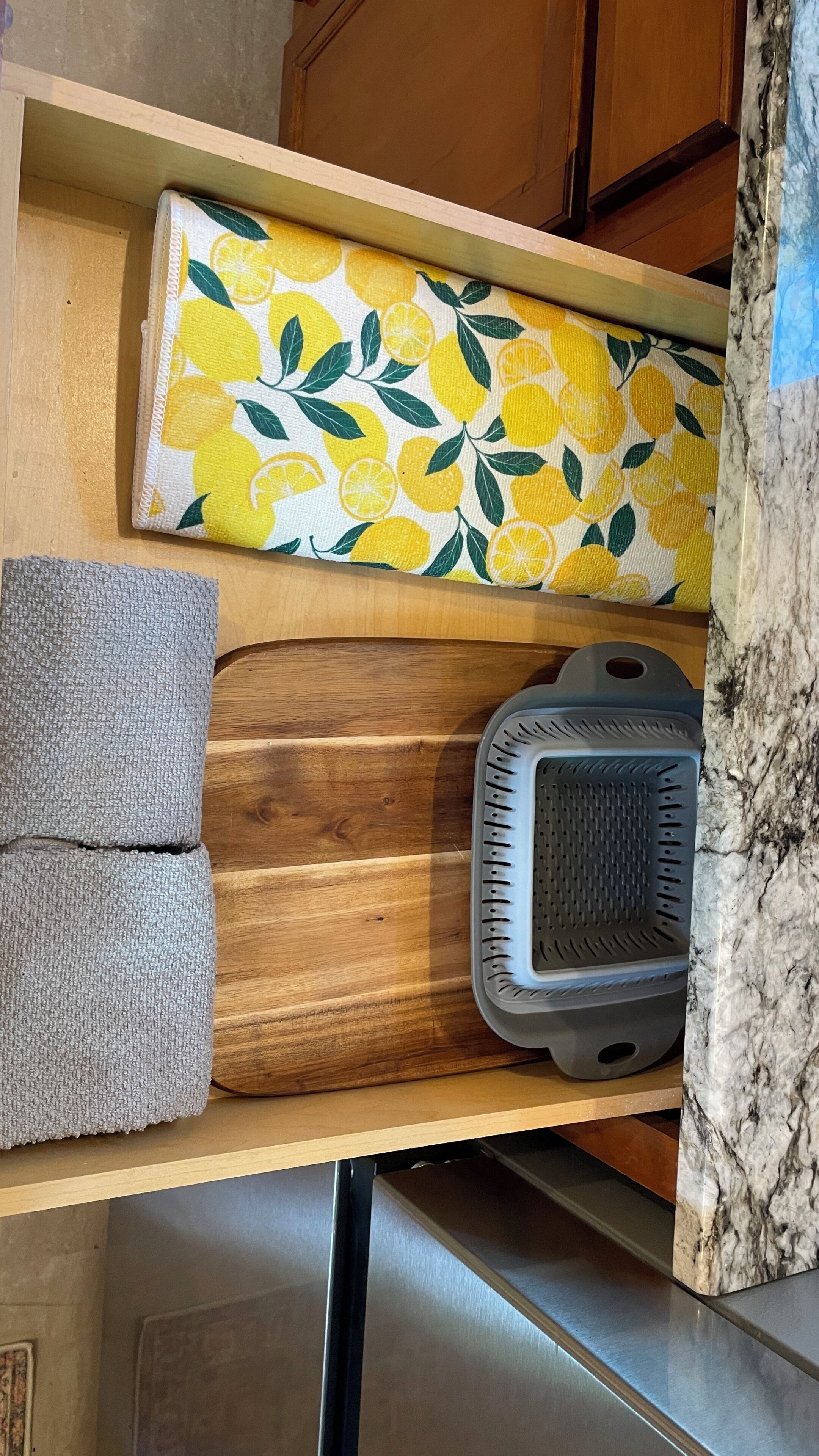 Eine Küche mit einer Holzausziehtisch, einer Tischdecke mit Zitronenblattmuster, einem grauen Handtuch und einem schwarzen Gerät.