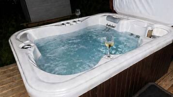 A hot tub with a wooden deck, a glass of wine, and a covered bench.