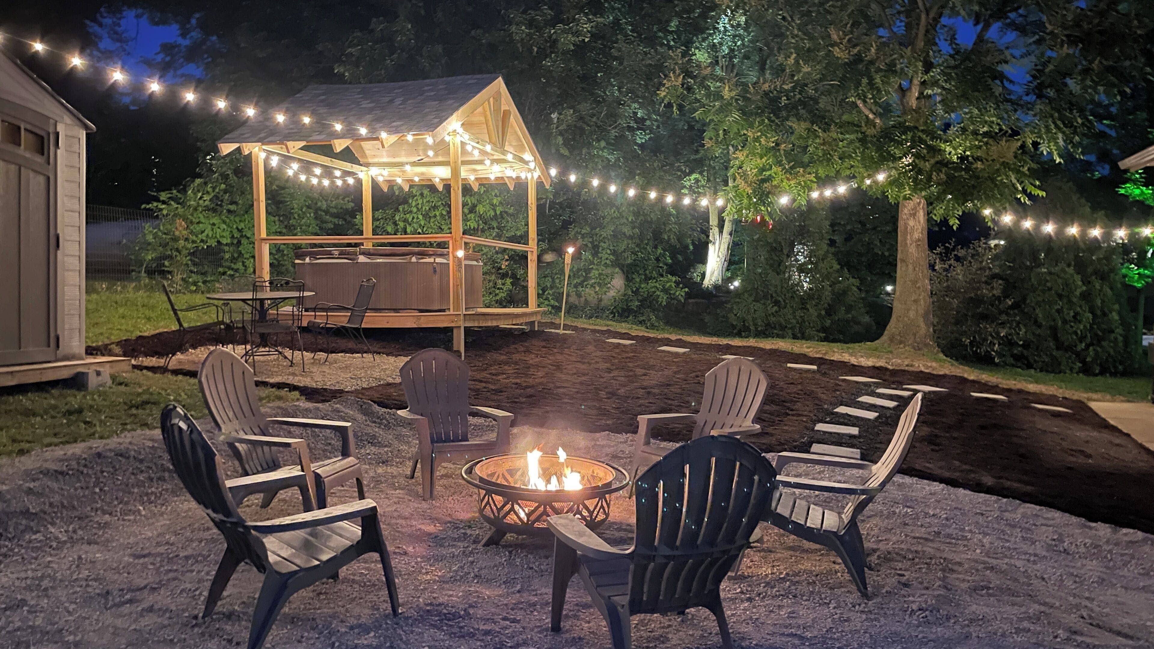 An outdoor seating area with Adirondack chairs, a fire pit, and a wooden pergola with string lights.