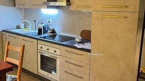 Een kleine keuken met een spoelbak, fornuis en kastjes.