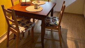 Een eetruimte met een houten tafel en stoelen, een raam met dunne gordijnen en een gele wand.