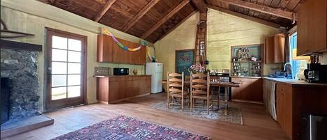 A spacious loft-style kitchen with wooden beams, a stone fireplace, and a large rug.