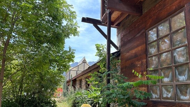 Un bâtiment rustique en bois, doté de grandes fenêtres et d’un chemin de jardin qui y mène.