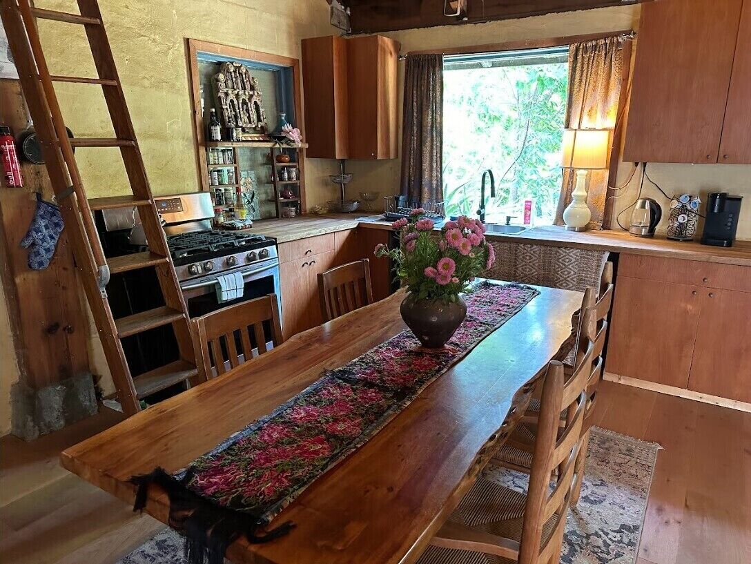 A rustic kitchen with wooden cabinets, a wooden dining table, and a vase with flowers.