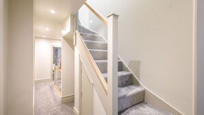 Un escalier moderne, avec des marches recouvertes de moquette et une rampe en verre, menant à l’étage supérieur.