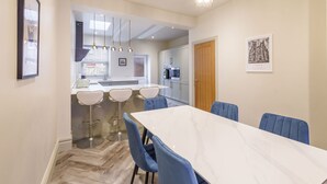 Une cuisine moderne avec des meubles blancs, un four encastré et un coin repas comprenant une table en marbre et des chaises bleues.