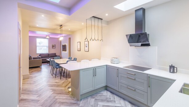 Une cuisine moderne dotée d’un grand îlot central, de meubles gris et de luminaires suspendus.