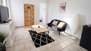 Un salon moderne avec un canapé noir, une bibliothèque en bois, une table basse et un grand lampadaire.