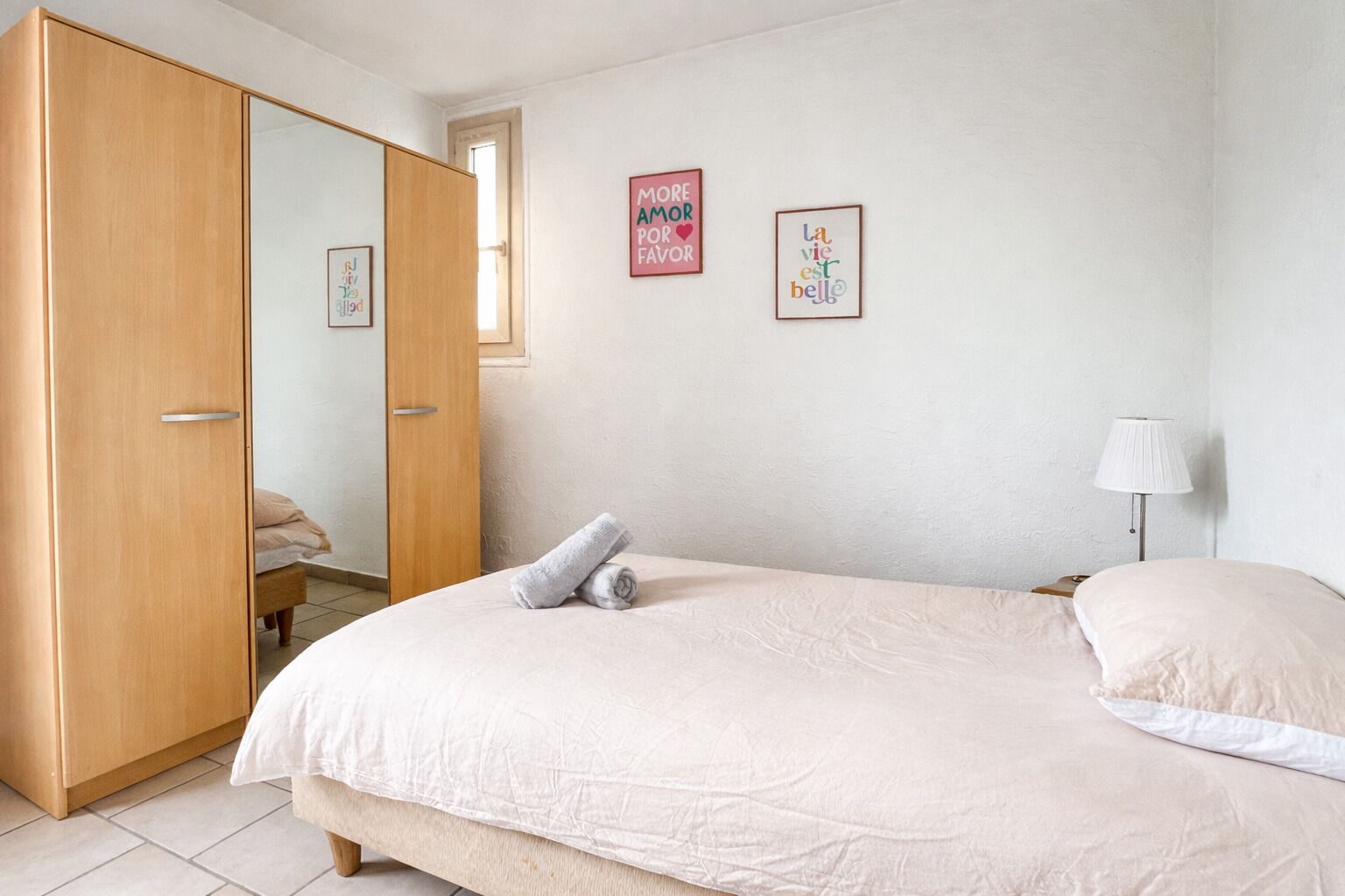 Ein Schlafzimmer mit einem Bett, einem Holzschrank, einer Nachttischlampe und zwei Wandbildern.