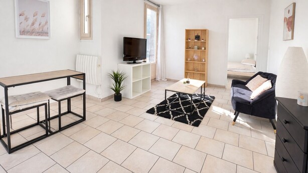 Un salon moderne avec un téléviseur, une bibliothèque en bois, un tapis noir et blanc et un canapé noir.