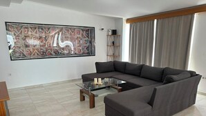 Ein modernes Wohnzimmer mit einem Ecksofa, einem Glastisch und einem großen abstrakten Gemälde an der Wand.