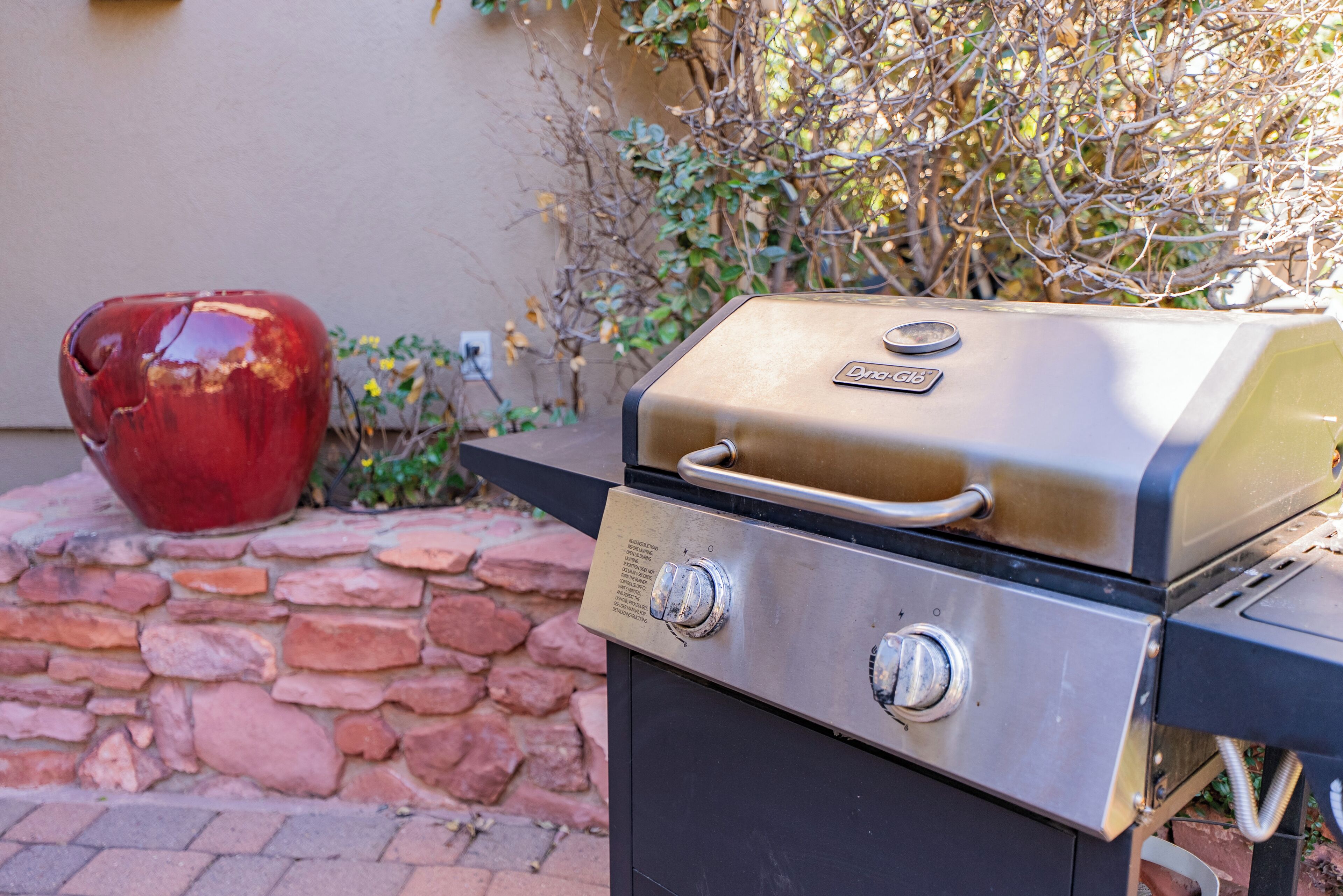 Una parrilla con panel de control, una maceta roja decorativa y una pared de piedra.