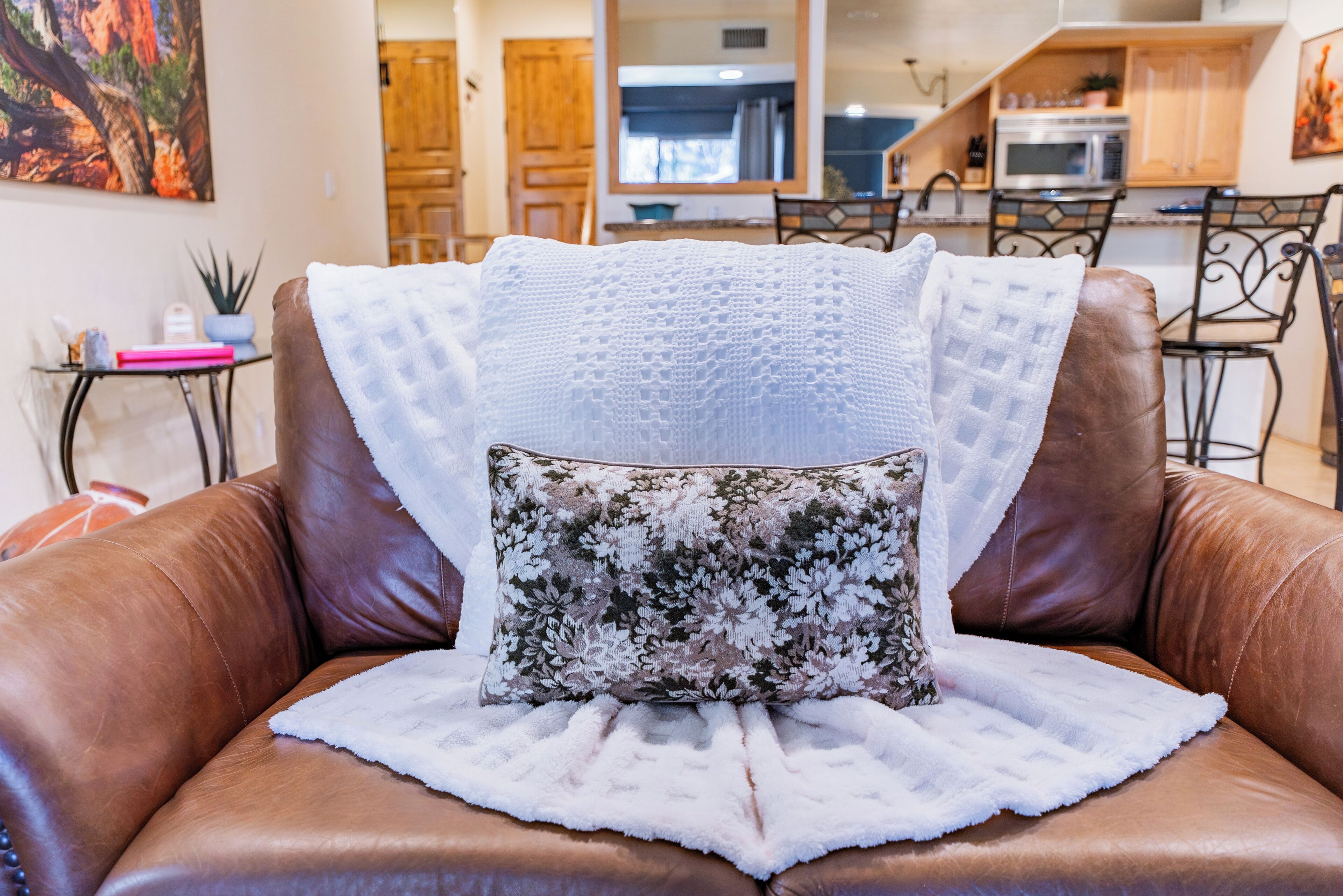 A brown leather sofa with a white throw blanket and a floral pillow.