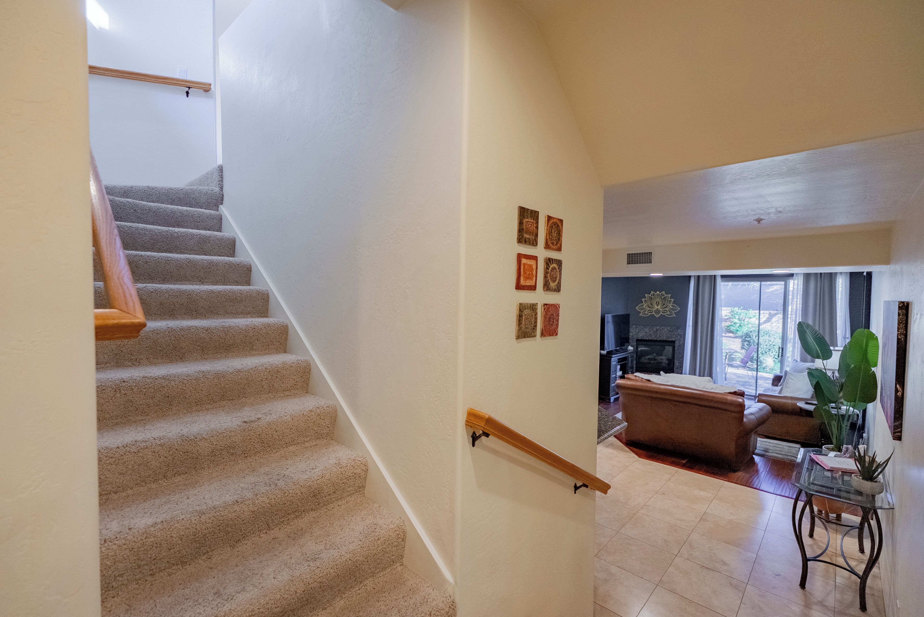 A carpeted staircase with a wooden handrail, a living room with a sofa, a coffee table, and a large plant.