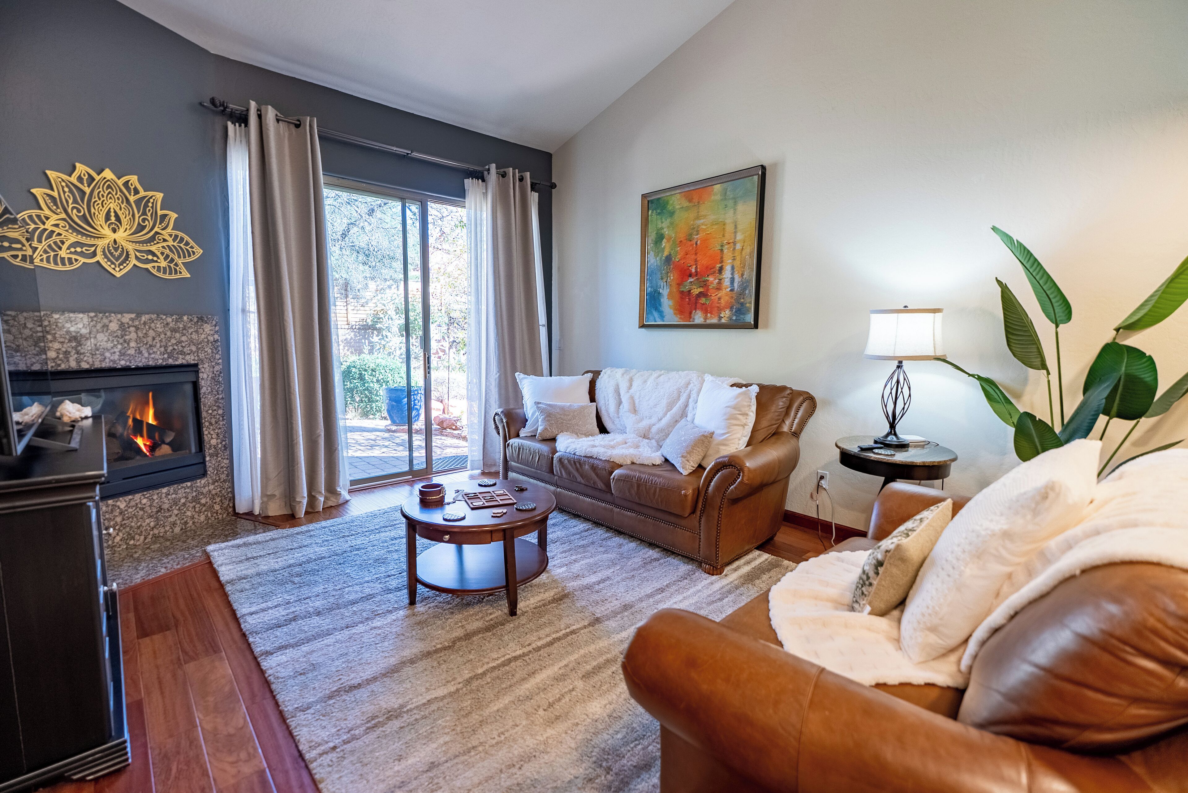 Un salon avec une cheminée, un canapé en cuir marron, une table basse et une grande fenêtre avec des rideaux.