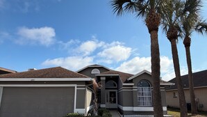 A residential house with a garage, a driveway, and a well-maintained lawn with palm trees. - Vintage nostalgic Orlando theme park looks for the perfect vacation destination! (Kissimmee)