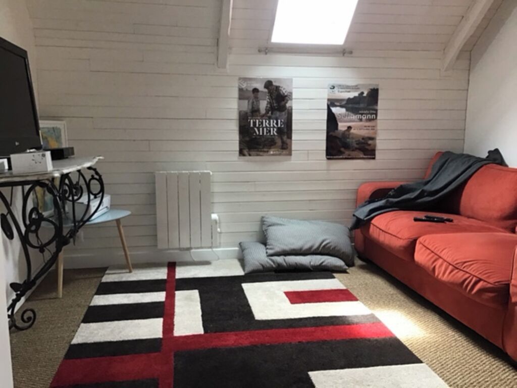 Um quarto com um sofá vermelho, um tapete com padrão preto e branco, um radiador e dois cartazes na parede.