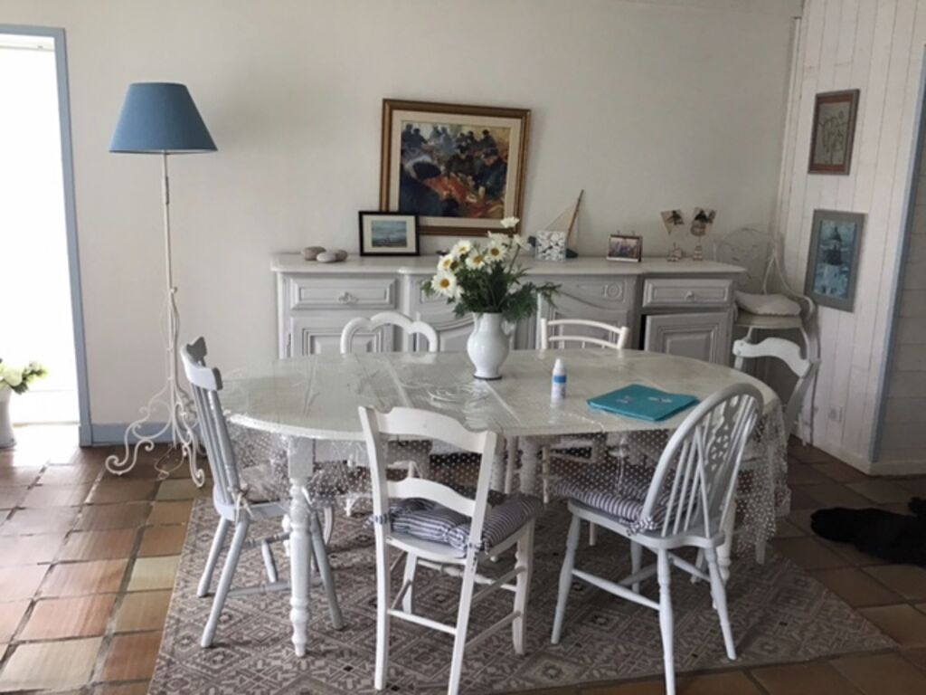 Un comedor con una mesa redonda, sillas blancas, un florero con flores y una lámpara.