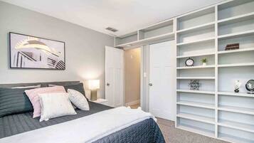 A bedroom with a bed, bedside tables, a nightstand, a wall-mounted artwork, and a built-in shelving unit.