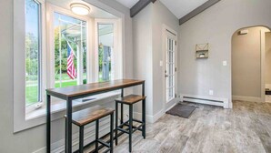 A modern kitchen with a wooden table and bar stools, large windows with an American flag, and a view of the outdoors.
