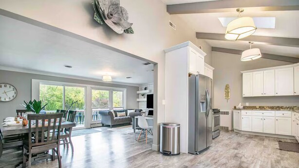 A spacious kitchen with white cabinets, a stainless steel refrigerator, and a dining area with a wooden table and chairs.